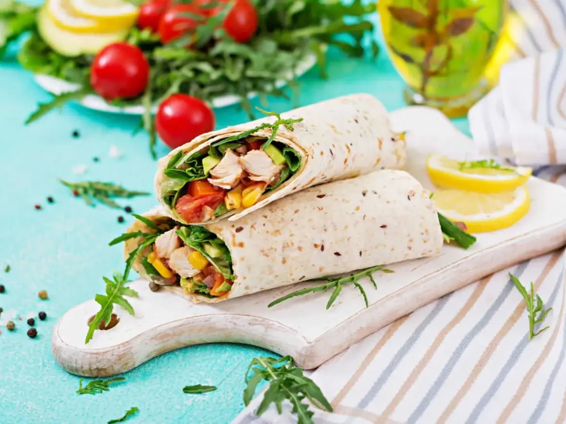 Deux wraps au poulet garnis de légumes frais, servis sur une planche en bois avec des quartiers de citron.