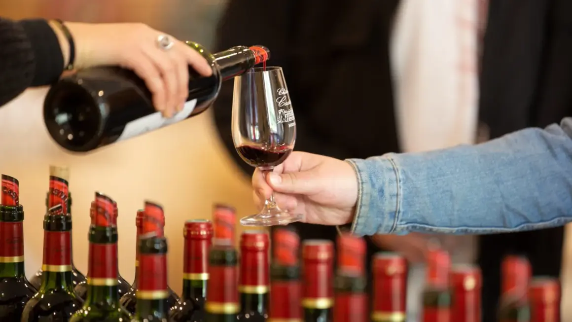 Service d'un vin rouge pour l'apéro, avec des bouteilles alignées en arrière-plan.