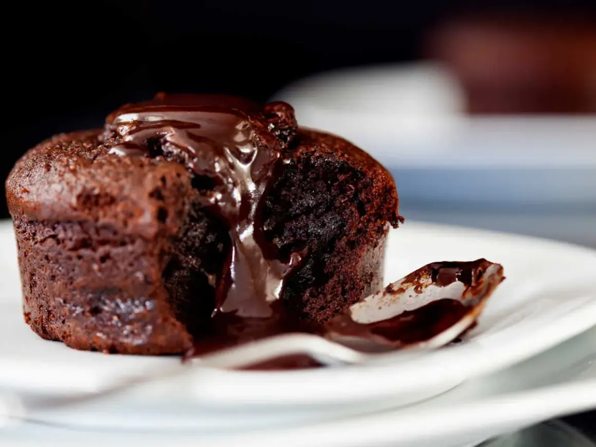 Un fondant au chocolat dégoulinant de sauce, une cuillère prête à savourer ce délice.