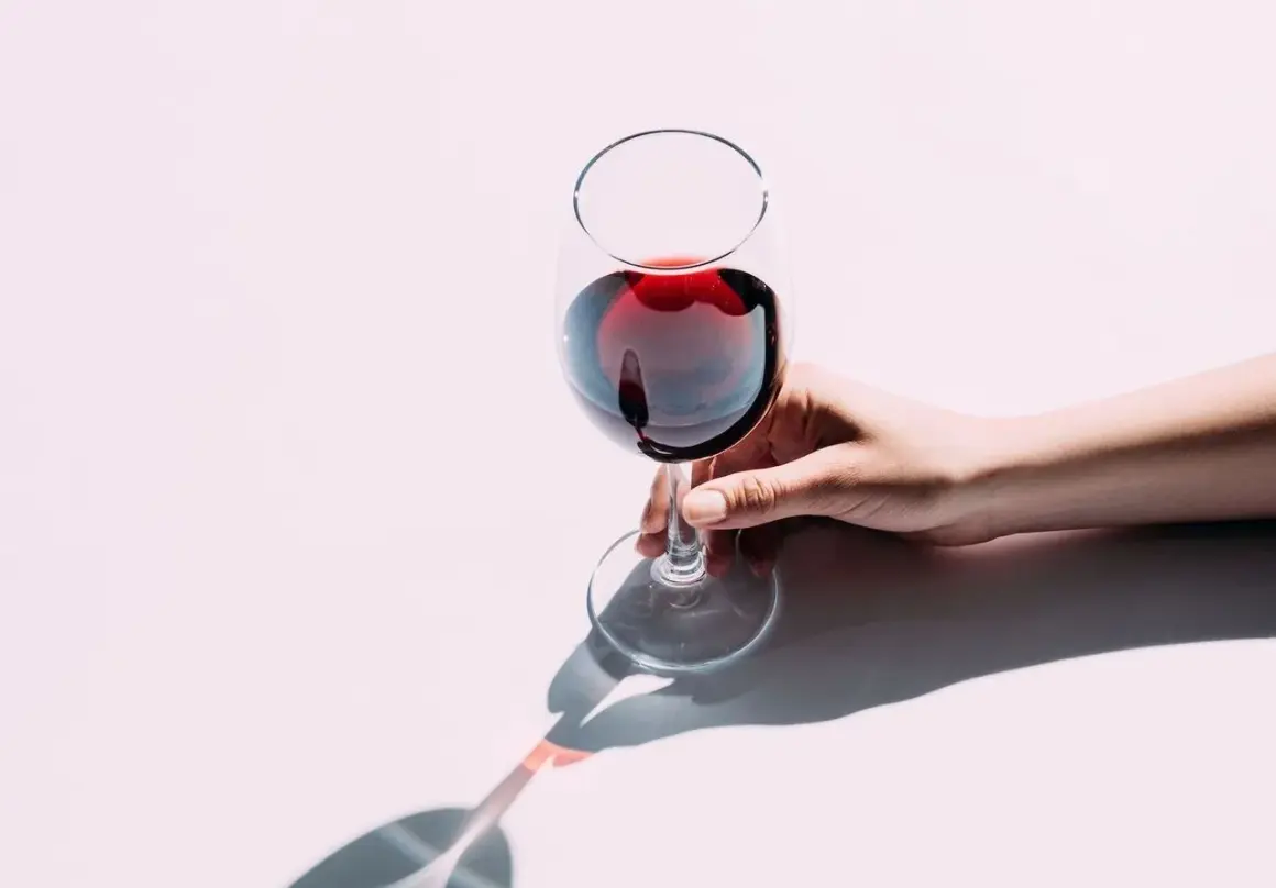 Une main tient délicatement un verre de vin rouge, le pouce et l'index sur le pied. Apprenez comment tenir un verre de vin pour en apprécier toutes les saveurs.
