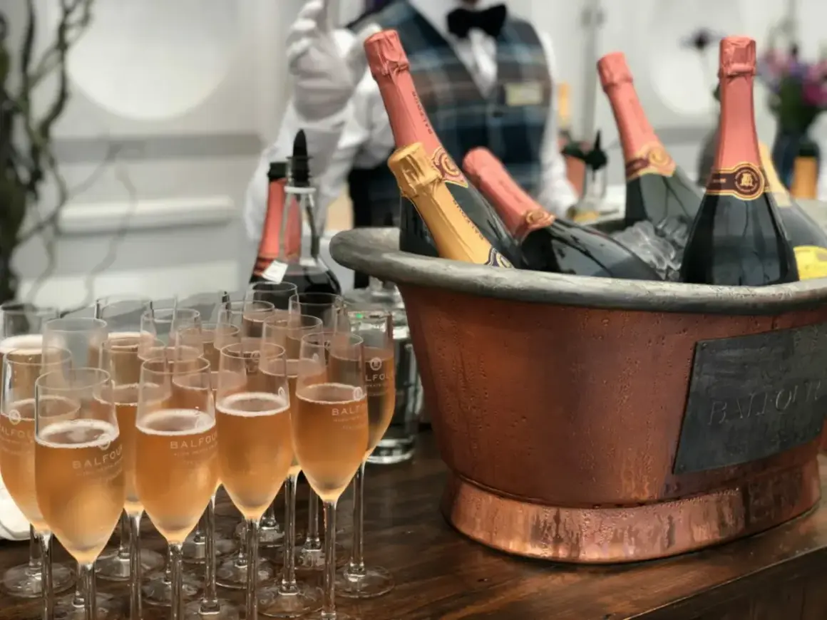 Une belle quantité de vin pour un mariage, avec des flûtes remplies de champagne et des bouteilles au frais dans un grand seau en cuivre.