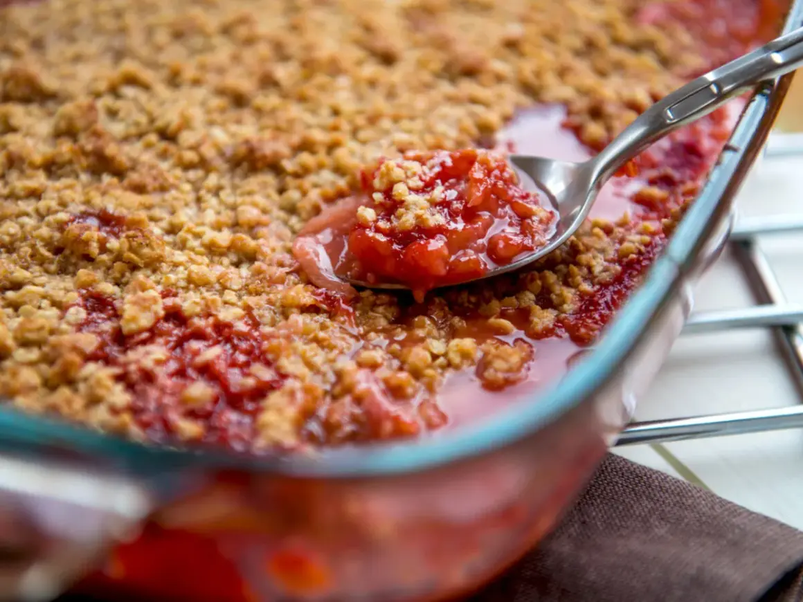 Une cuillère prélève une portion généreuse de crumble rhubarbe, révélant la garniture fruitée et croustillante.