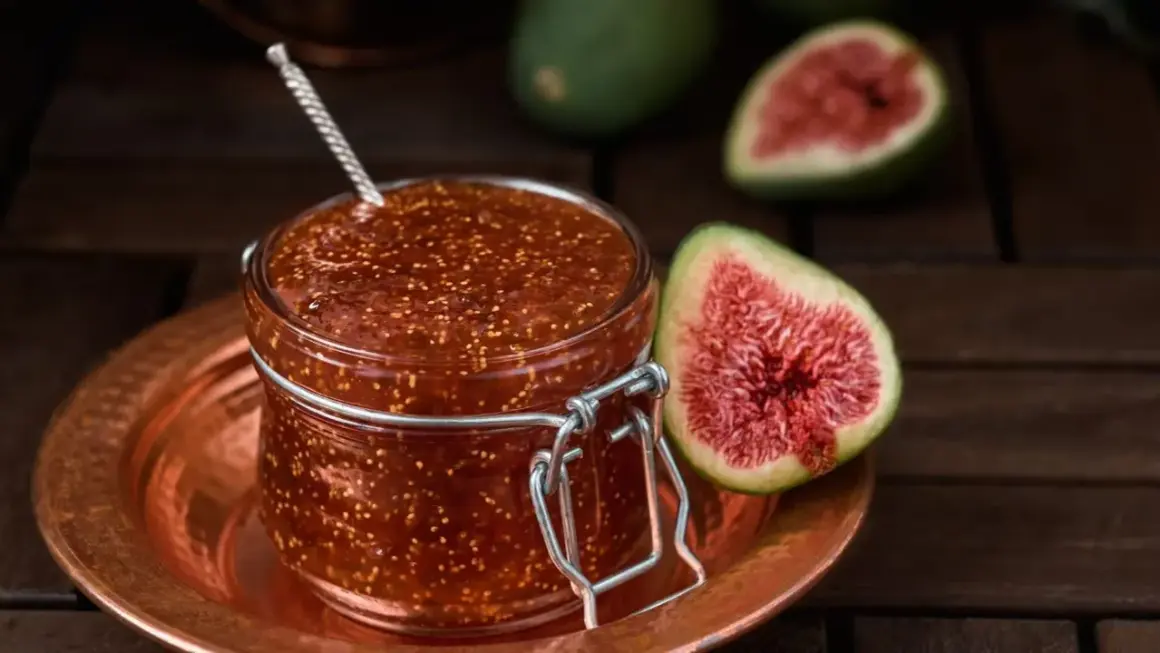 Un bocal de confiture de figues maison, avec des figues fraîches coupées en deux à côté.