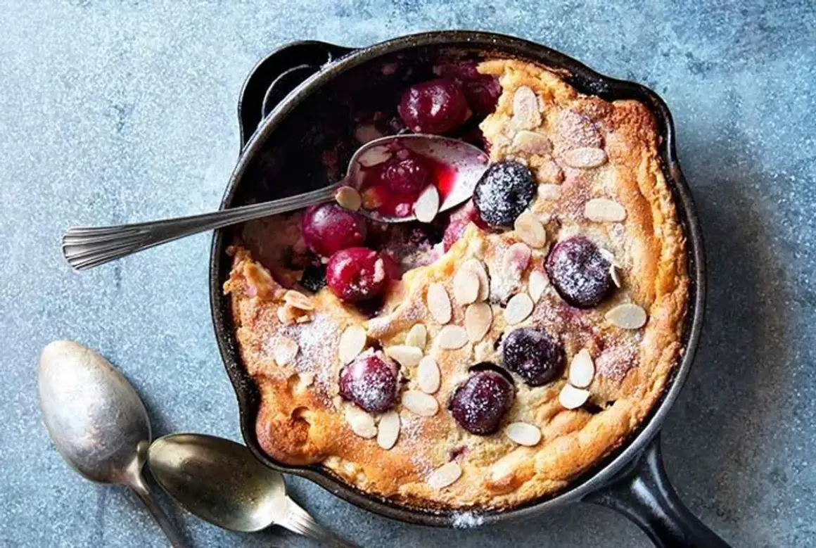 Clafoutis aux cerises dans une poêle, saupoudré de sucre glace et d'amandes effilées. Une recette clafoutis facile et gourmande.