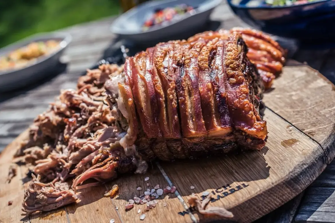 Un morceau de porc rôti avec une couenne croustillante et un effiloché de porc savoureux sur une planche en bois.