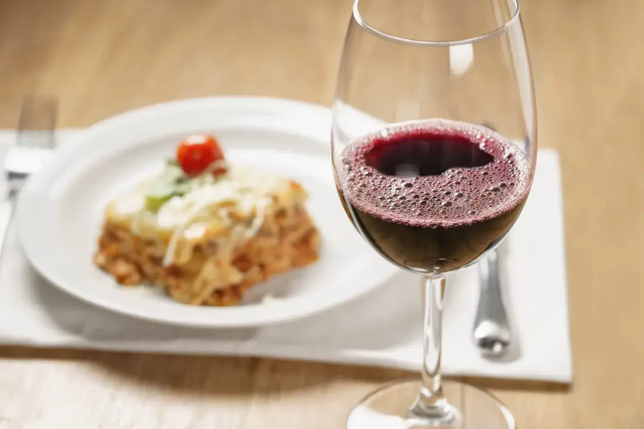 Un verre de vin rouge p&eacute;tillant &agrave; c&ocirc;t&eacute; d'une part de lasagnes savoureuse. La question est : quel vin avec des lasagnes pour un repas parfait ?