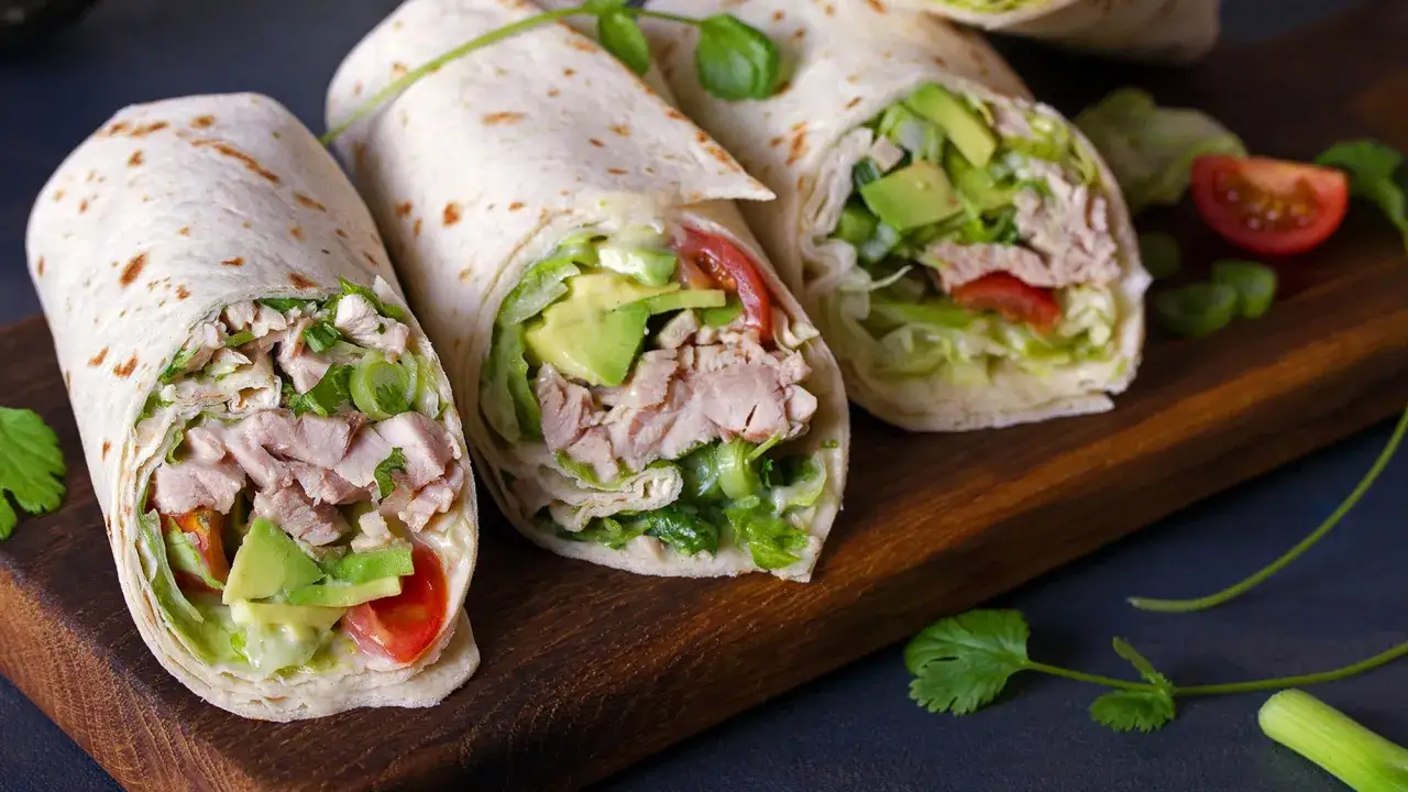 Trois wraps poulet savoureux garnis d'avocat, de tomates et de laitue, pr&eacute;sent&eacute;s sur une planche en bois.