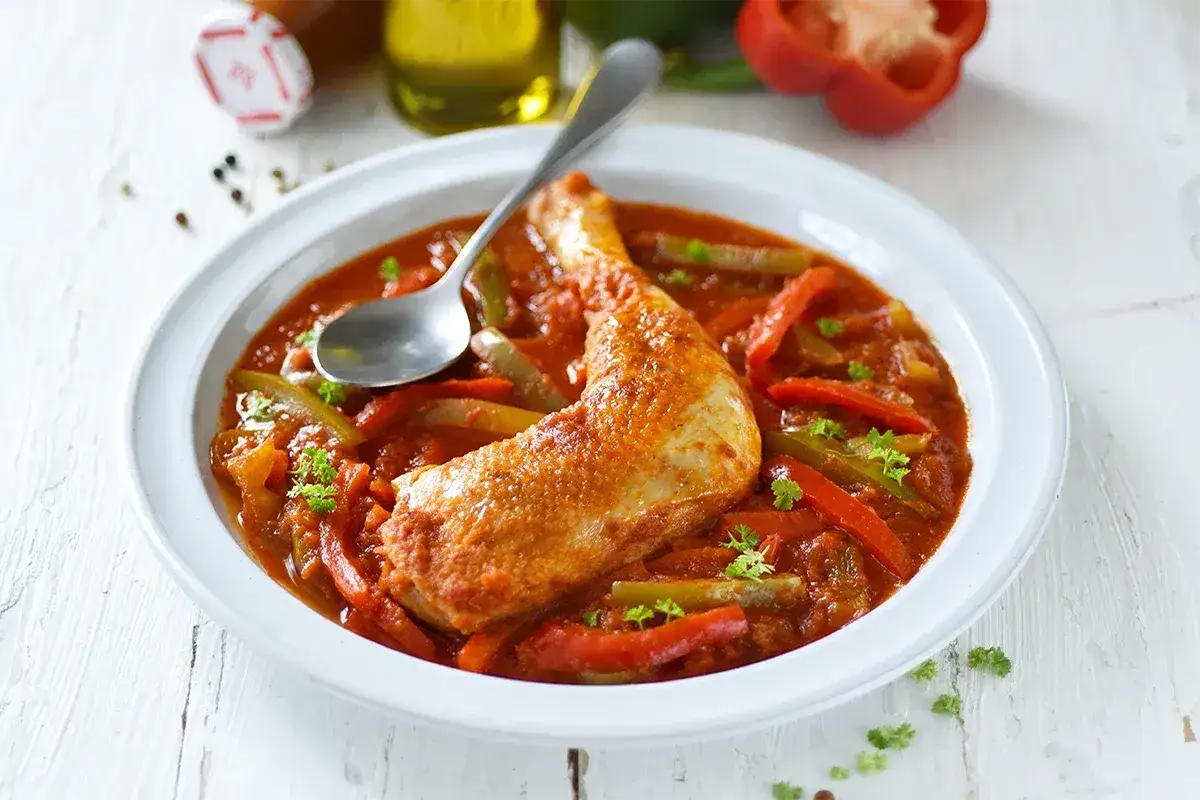 Un plat de poulet basquaise savoureux, id&eacute;al pour se demander quel vin avec poulet basquaise. Servi dans une assiette blanche avec une cuill&egrave;re.