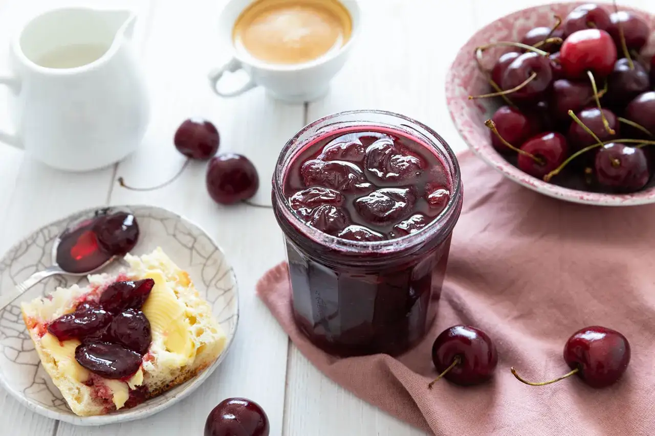 Un pot de confiture de cerises maison, des cerises fraîches et une tartine beurrée. Un délice pour le petit-déjeuner.