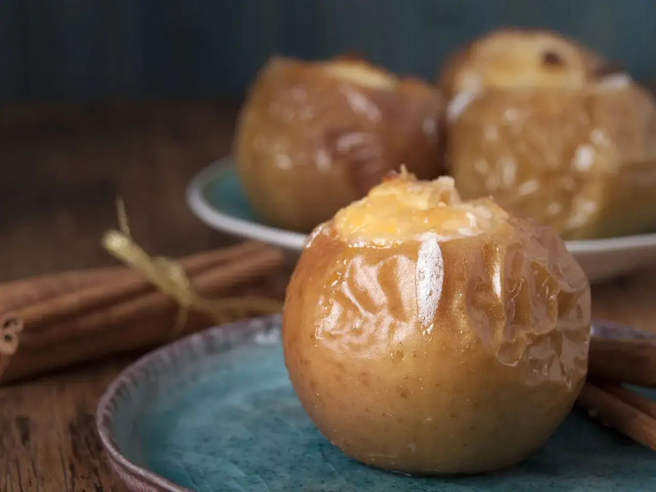 Trois pommes au four dorées et caramélisées, garnies d'une touche de cannelle, sur des assiettes bleues. Un délice réconfortant.