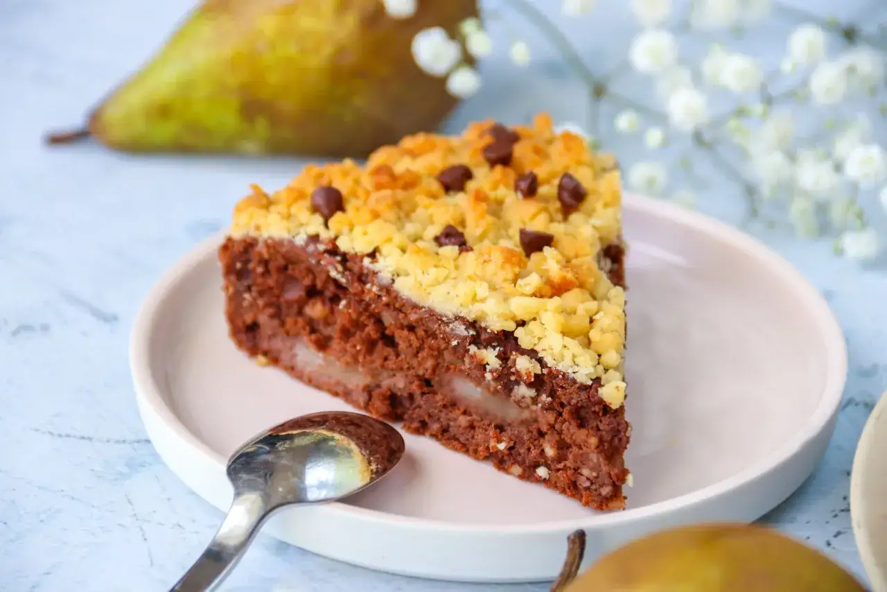Tranche de crumble poire chocolat, garnie de p&eacute;pites de chocolat, sur une assiette rose avec une cuill&egrave;re.