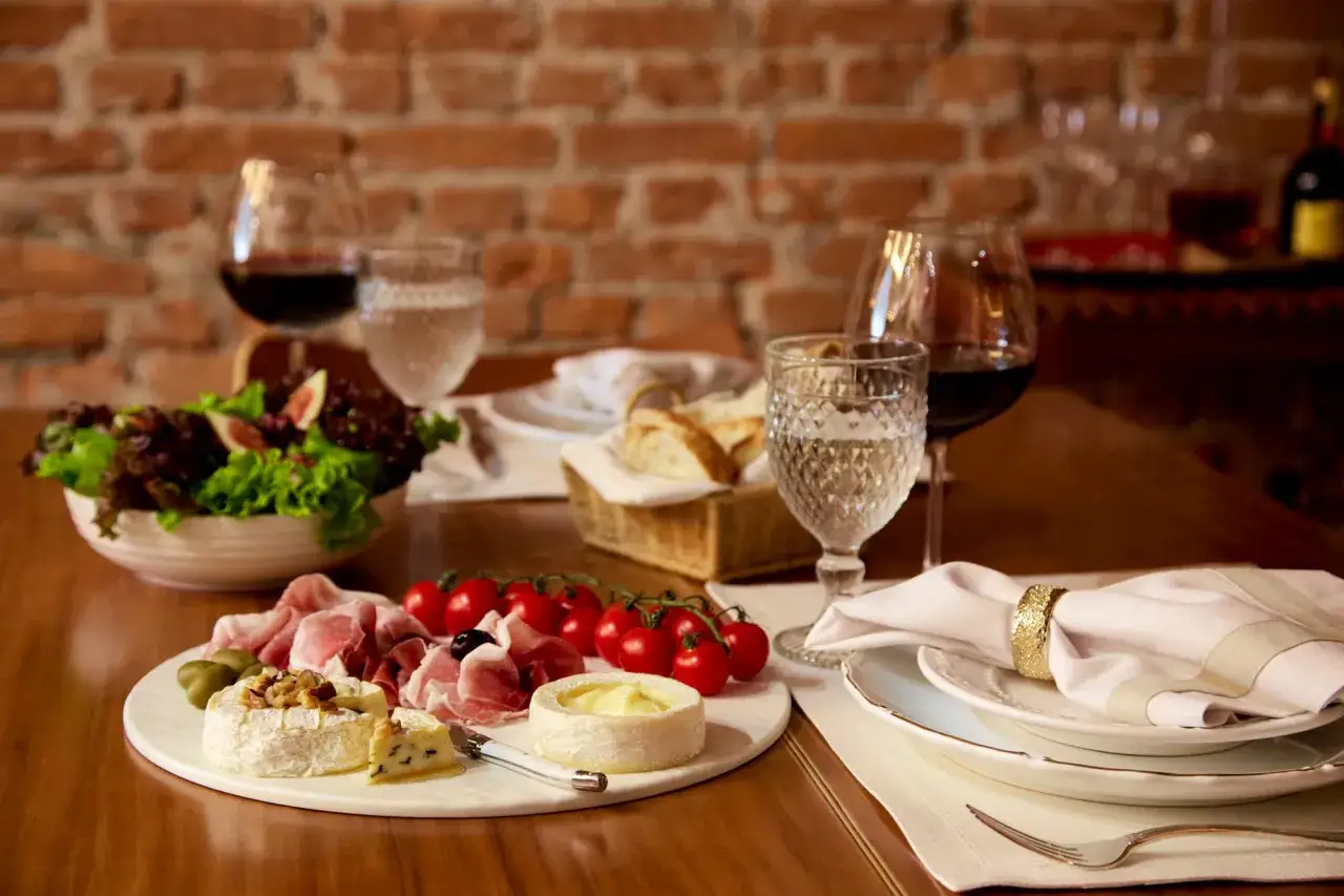 Plateau de fromages, charcuterie, tomates cerises et salade. Un verre de vin rouge sugg&egrave;re quel vin avec le fromage pour un repas parfait.