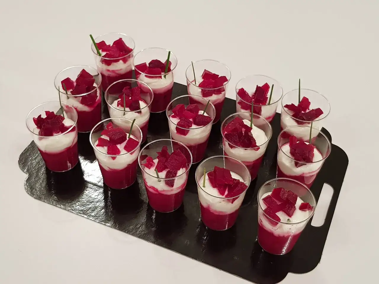 Douze verrines betterave et crème, garnies de dés de betterave et d'une tige de ciboulette, présentées sur un plateau noir.