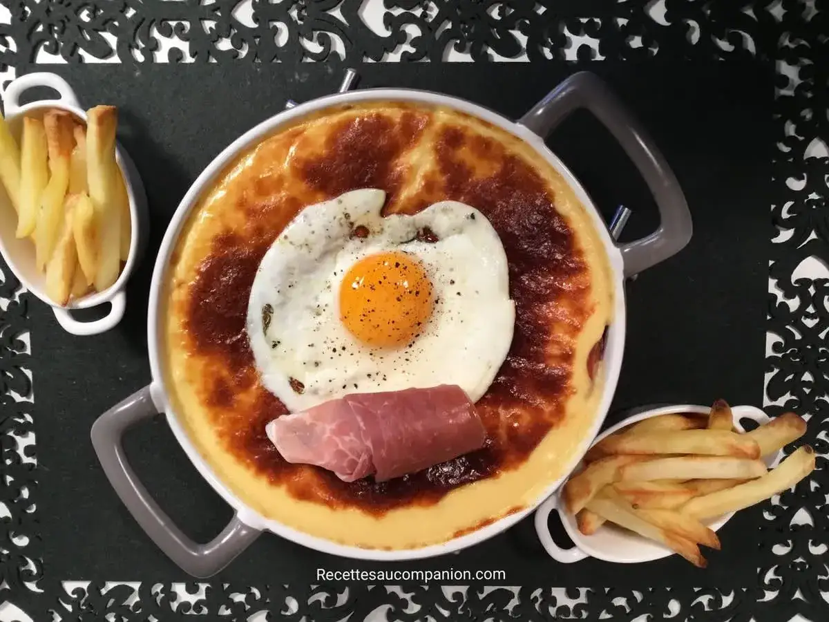Un plat de recette welsh gratiné, surmonté d'un œuf au plat et d'une tranche de jambon, accompagné de frites croustillantes.
