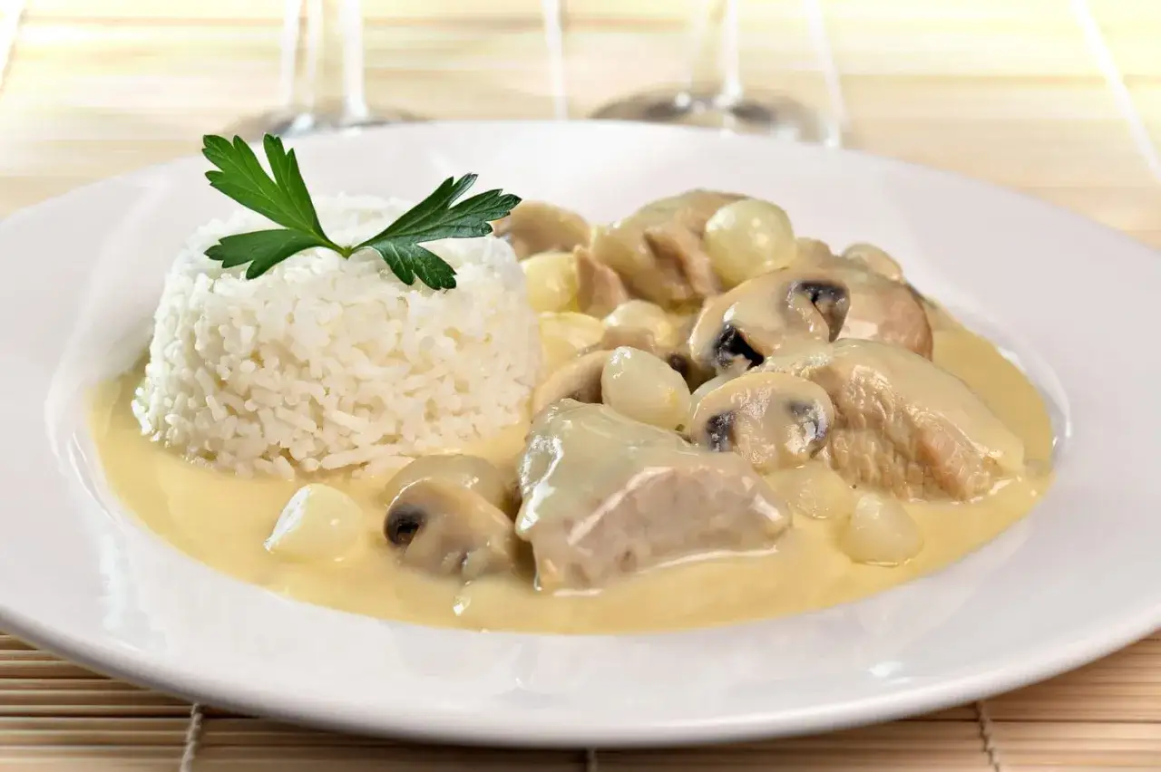 Une assiette de blanquette de veau cr&eacute;meuse avec des champignons et des oignons, servie avec une timbale de riz blanc garnie de persil.