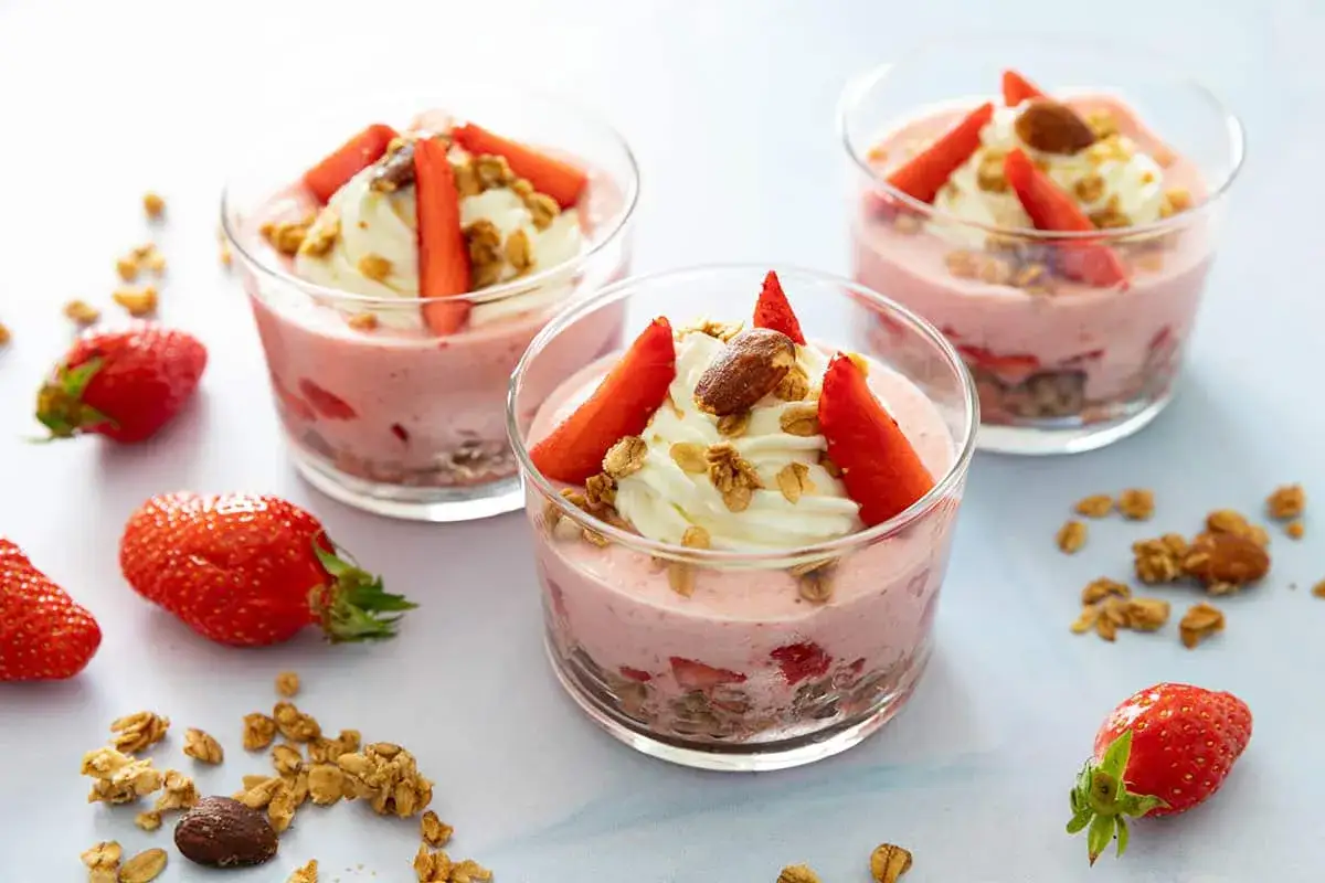 D&eacute;licieuse mousse fraise avec cr&egrave;me fouett&eacute;e, granola et amandes, servie dans des verres.