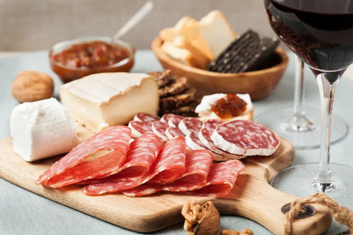 Un verre de vin rouge accompagne un plateau de charcuterie, fromages, pain et confiture. Parfait pour un ap&eacute;ro gourmand.