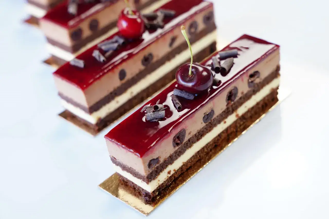 Gourmandise de la for&ecirc;t noire : g&acirc;teaux au chocolat, cr&egrave;me et cerises, napp&eacute;s d'un gla&ccedil;age rouge vif et d&eacute;cor&eacute;s de copeaux de chocolat.