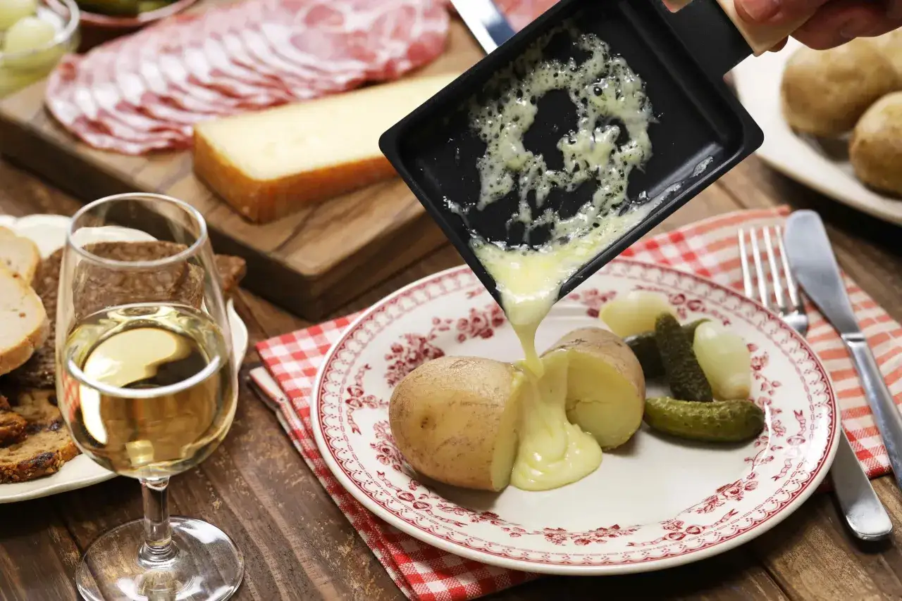 Un verre de vin raclette blanc accompagne des pommes de terre et des cornichons, avec du fromage fondu vers&eacute; dessus.