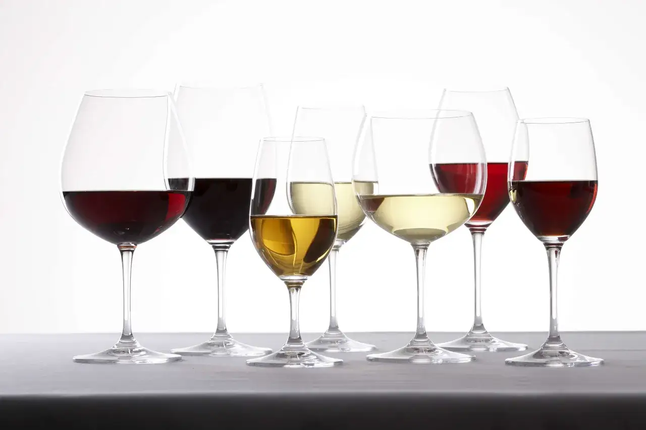 Plusieurs verres de vin rouge couleur, certains avec du vin blanc, sur un fond clair.