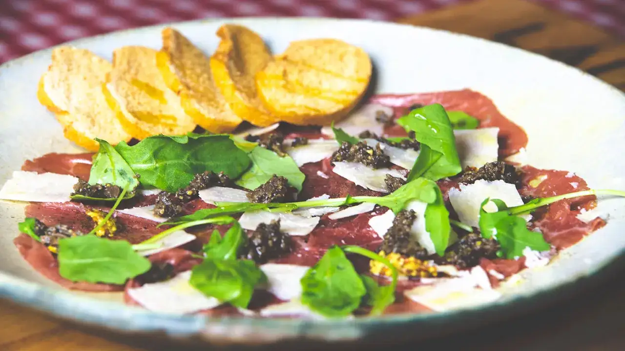 D&eacute;licieux carpaccio de boeuf, fines tranches de viande crue garnies de roquette, copeaux de parmesan et d'une touche de moutarde. Servi avec des toasts grill&eacute;s.