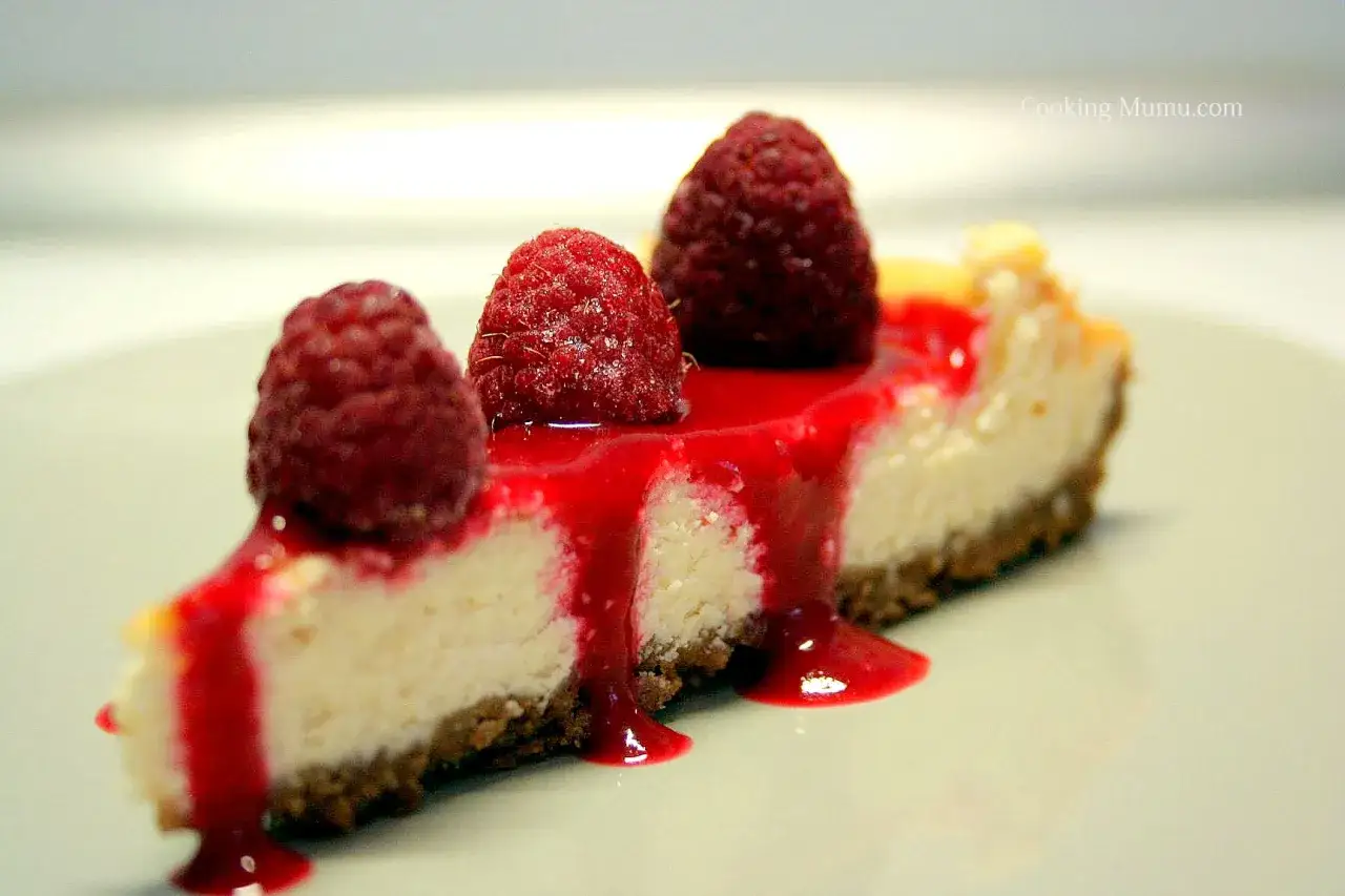 Tranche de cheesecake garnie de framboises fraîches et nappée d'un coulis de framboise onctueux.