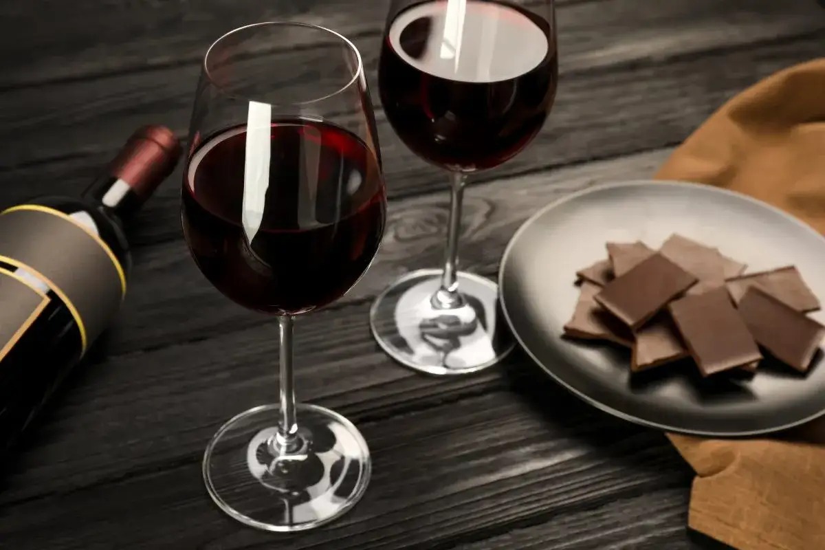 Bouteille de vin rouge, deux verres de vin et une assiette de chocolat sur une table en bois.