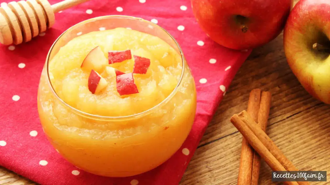 Un verre de compote de pommes maison, garni de dés de pommes rouges, sur une serviette à pois. Des pommes et des bâtons de cannelle sont à proximité.
