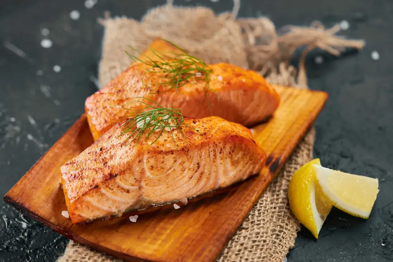 Deux pavés de saumon grillé, ornés d'aneth et de gros sel, servis sur une planche en bois avec des quartiers de citron. Un délice pour accompagner un bon vin.