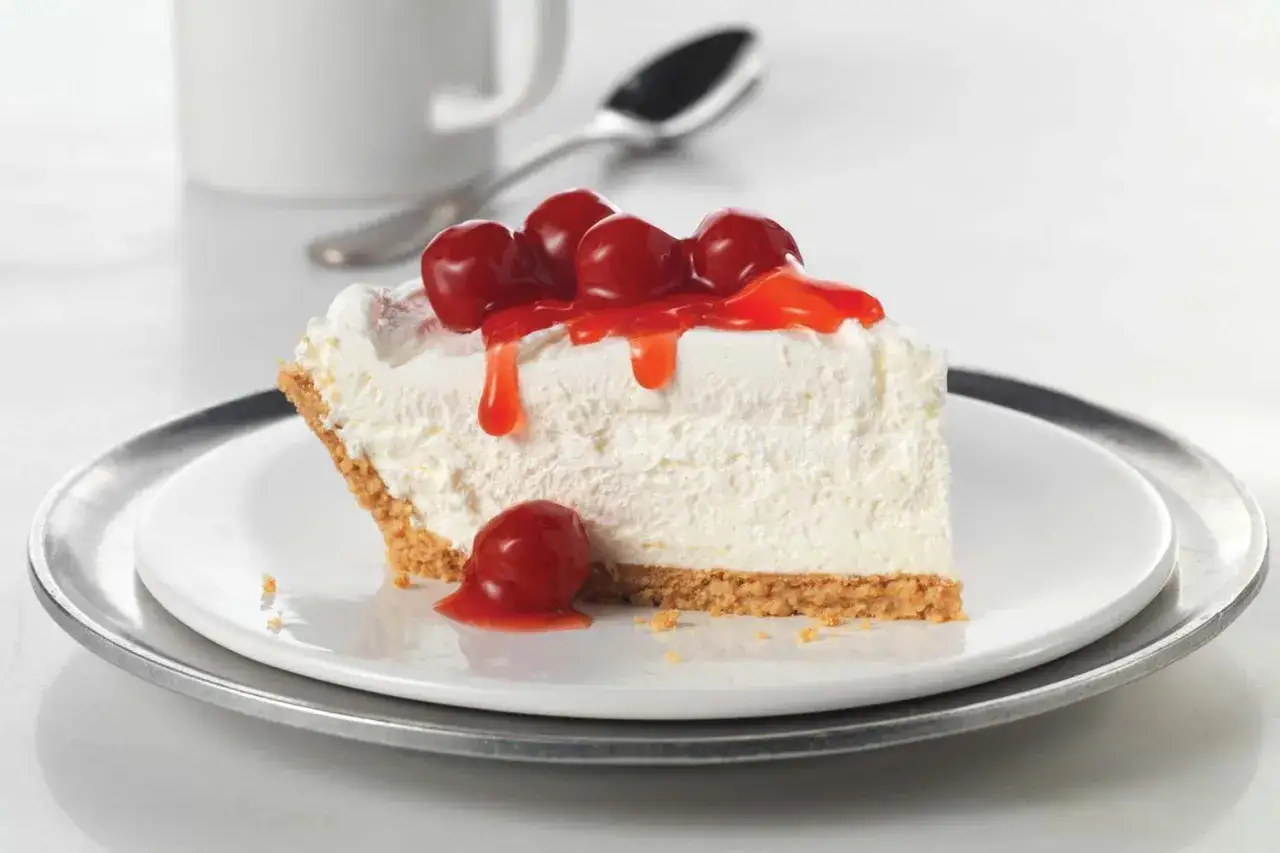 Tranche de cheesecake sans cuisson, garnie de cerises et de coulis rouge, sur une assiette blanche.