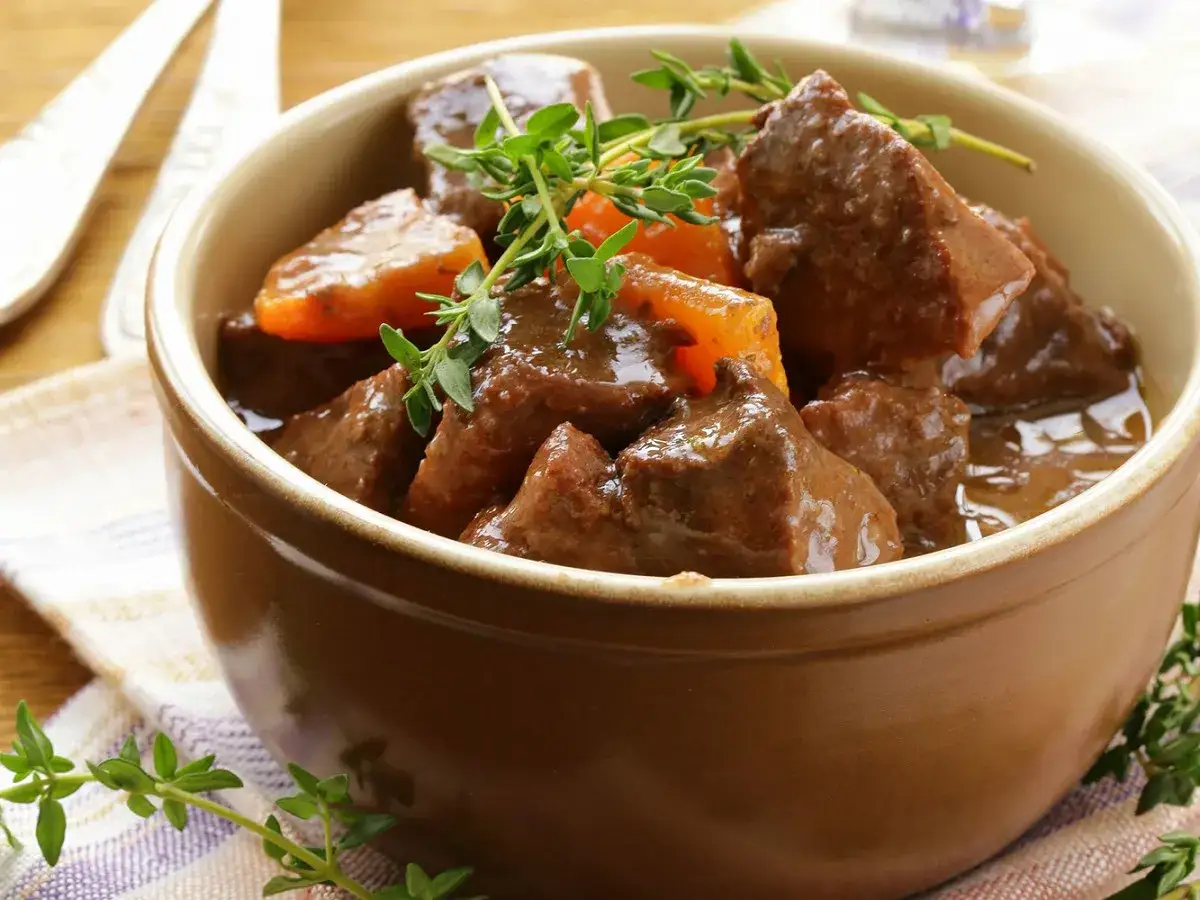 Un plat r&eacute;confortant de boeuf carottes mijot&eacute;, garni de thym frais, servi dans un bol en terre cuite.