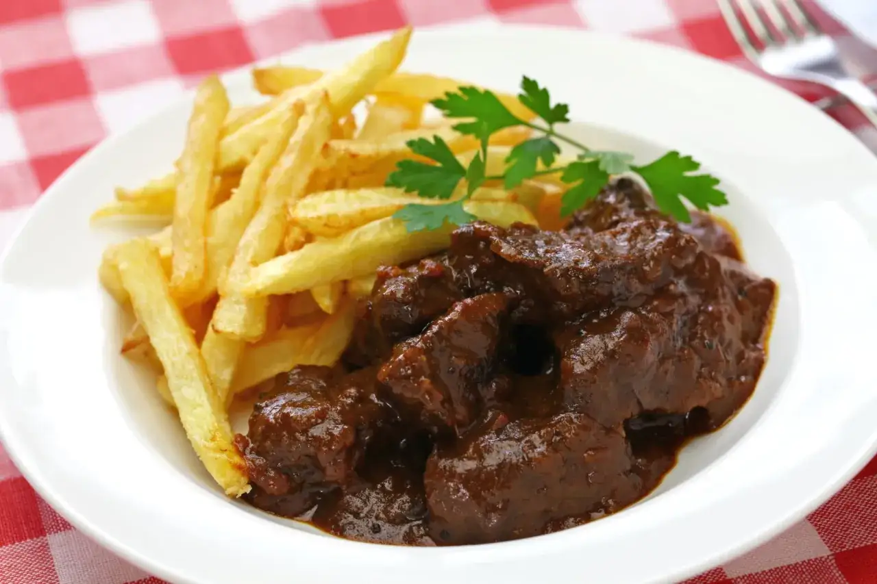 Une assiette de carbonade flamande, un plat mijoté de bœuf à la bière, servi avec des frites dorées et une touche de persil frais.