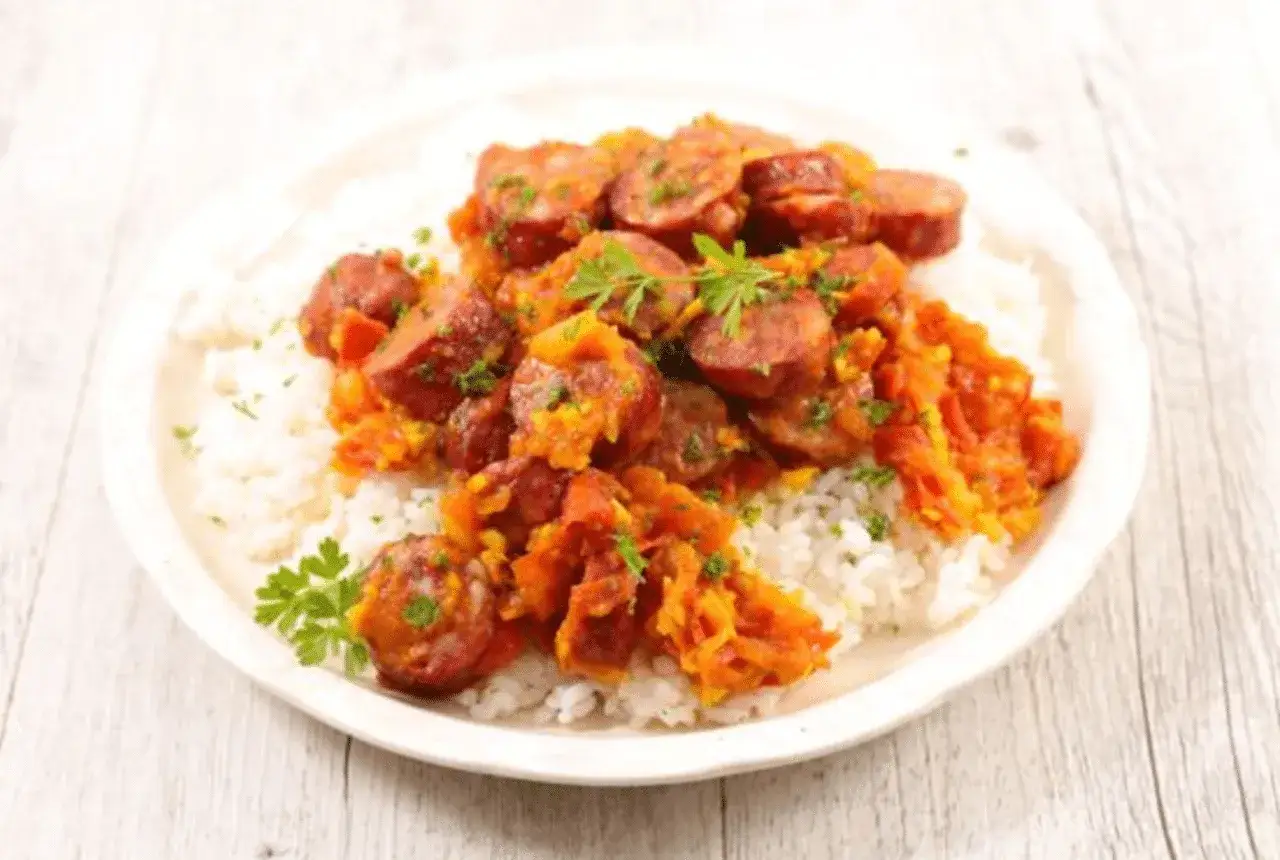 Un plat de rougail saucisse savoureux, avec des rondelles de saucisses épicées sur un lit de riz blanc, garni de persil frais.