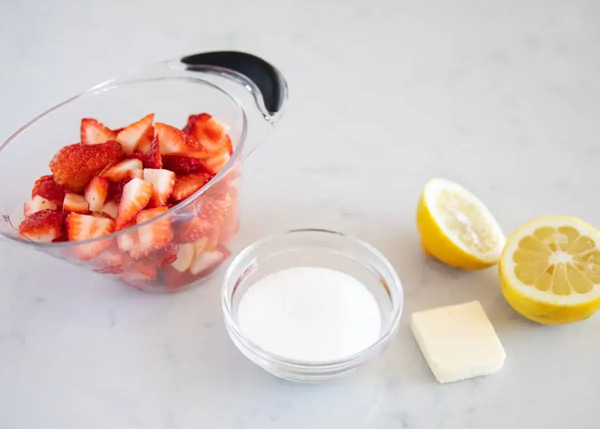 Ingr&eacute;dients pour un coulis de fraise : fraises coup&eacute;es, sucre, beurre et citrons coup&eacute;s en deux.