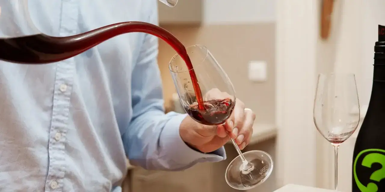 Un homme verse un vin trouble d'une carafe dans un verre. Une bouteille de vin est &agrave; c&ocirc;t&eacute;.