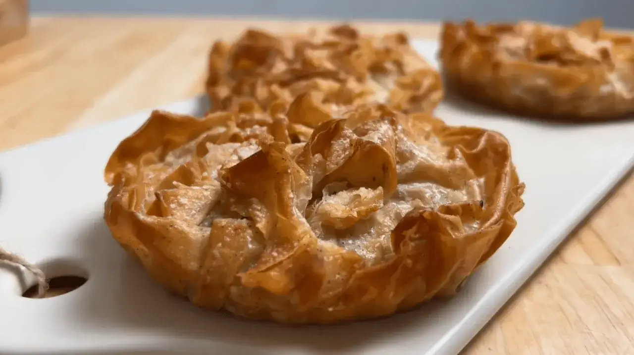 Trois d&eacute;licieux clafoutis aux pommes individuels, dor&eacute;s et croustillants, sur une assiette blanche.