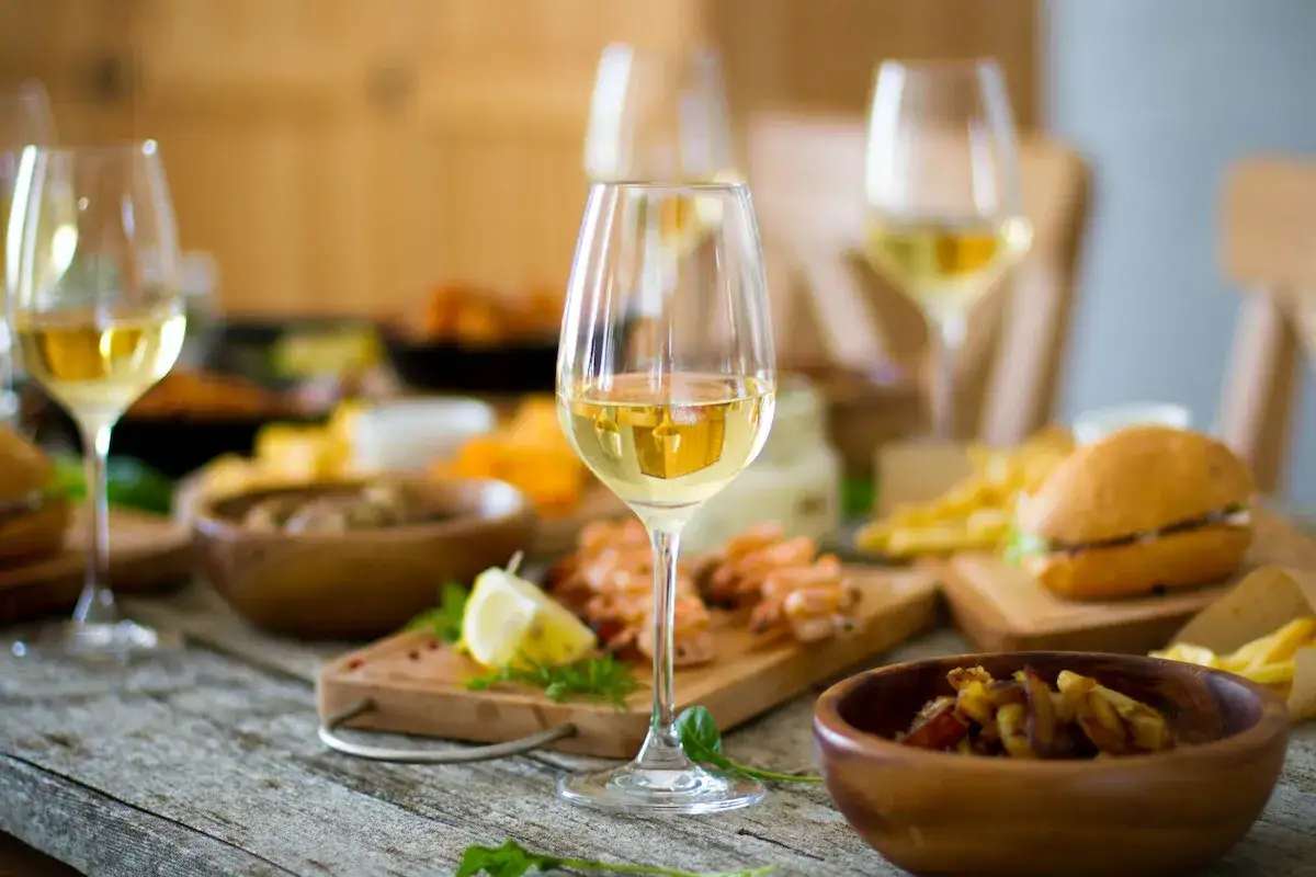 Verre de vin blanc pour apero, accompagné de crevettes, frites et mini-burgers sur une table en bois.