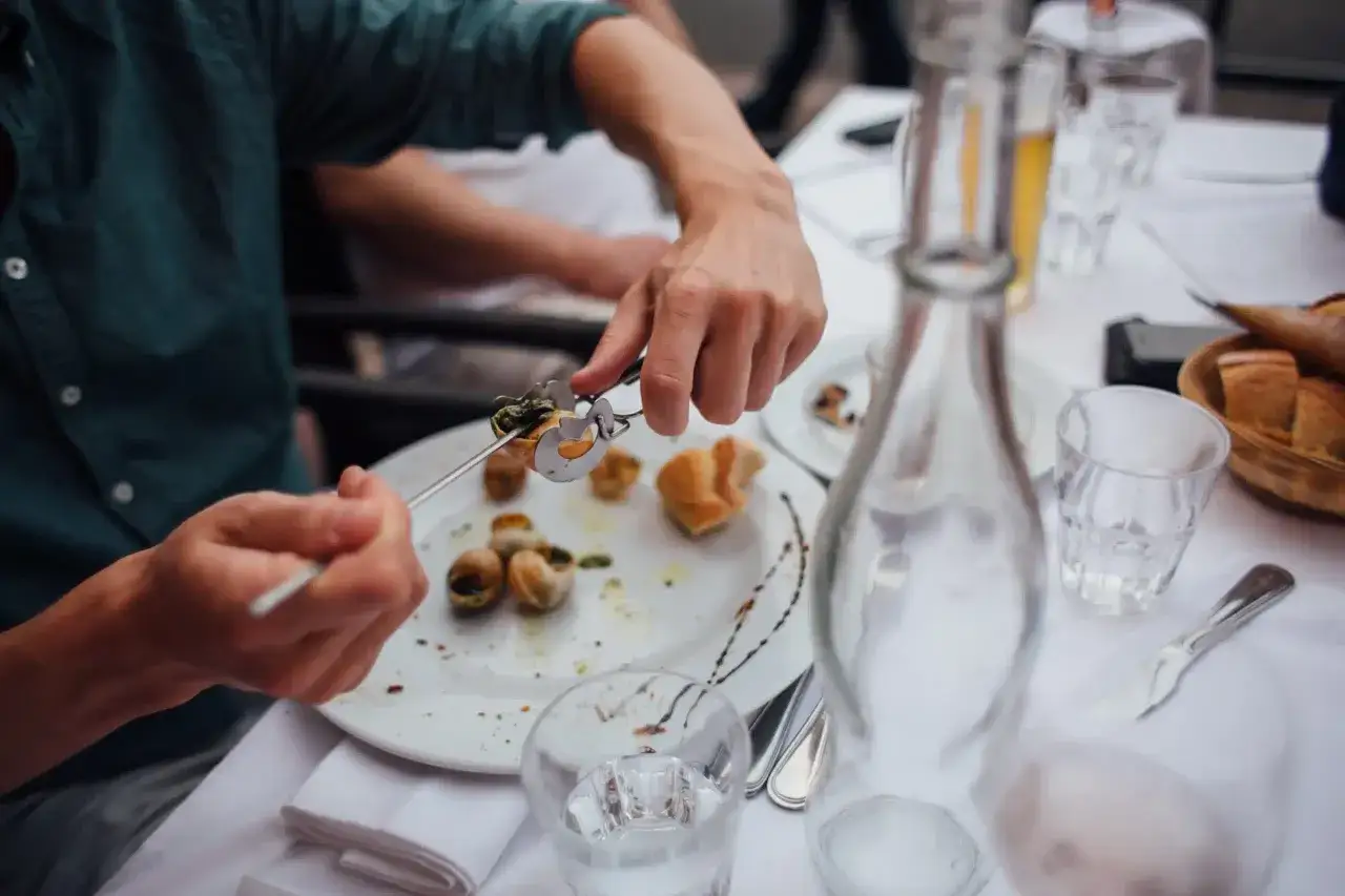 Un homme d&eacute;guste des escargots, une question se pose : quel vin avec les escargots ? Une carafe et du pain compl&egrave;tent ce repas.