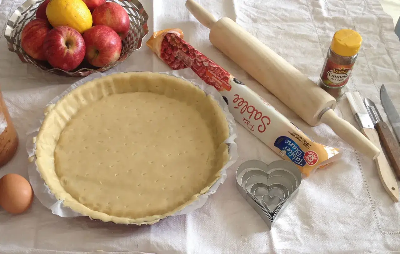 Pr&eacute;paration d'une tarte aux pommes : p&acirc;te sabl&eacute;e, pommes, rouleau, &oelig;uf, cannelle et emporte-pi&egrave;ces en forme de c&oelig;ur.