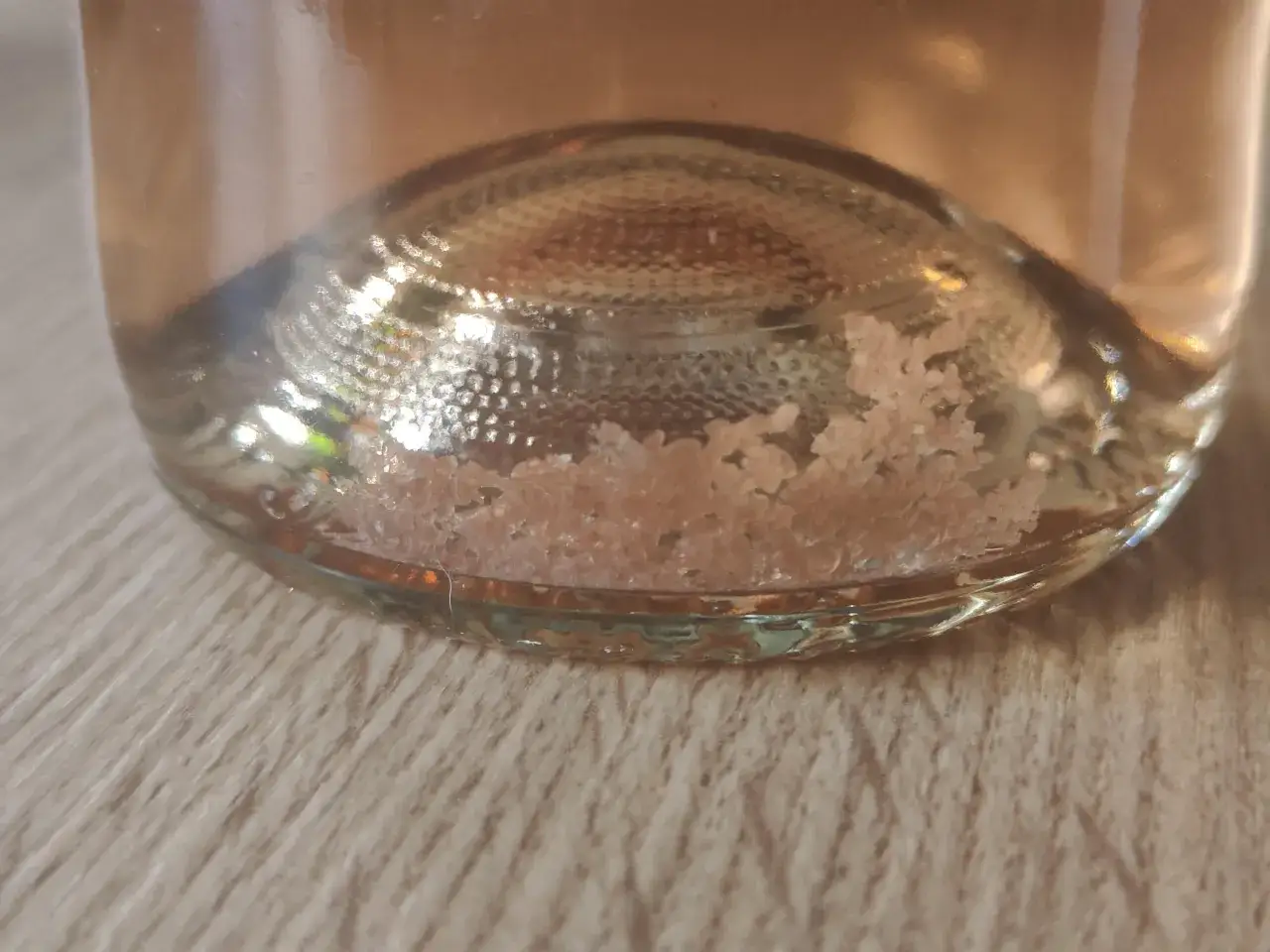 Gros plan sur le fond d'une bouteille de vin blanc, r&eacute;v&eacute;lant un d&eacute;p&ocirc;t cristallin rose p&acirc;le.