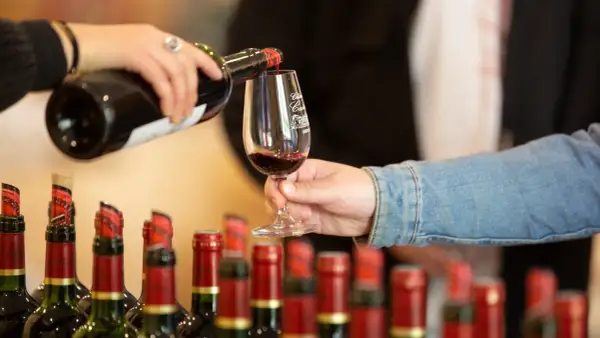 Service d'un vin rouge pour l'apéro, avec des bouteilles alignées en arrière-plan.