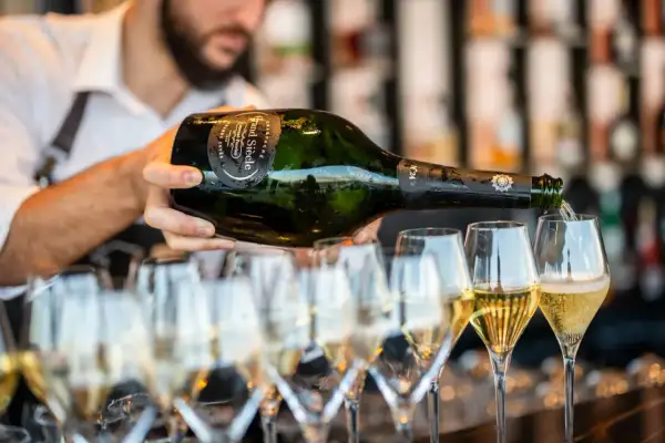 Un serveur verse du champagne d'une bouteille magnum dans plusieurs flûtes. La quantité de champagne est généreuse.