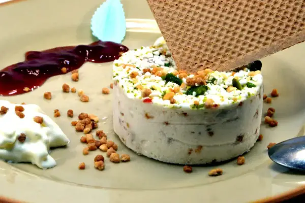 Un délicieux nougat glacé, parsemé de fruits secs et de pistaches, servi avec une touche de coulis de fruits rouges et une gaufrette croustillante.