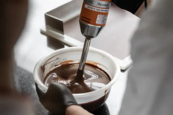 Un mixeur plongeant prépare une onctueuse ganache chocolat dans un bol.