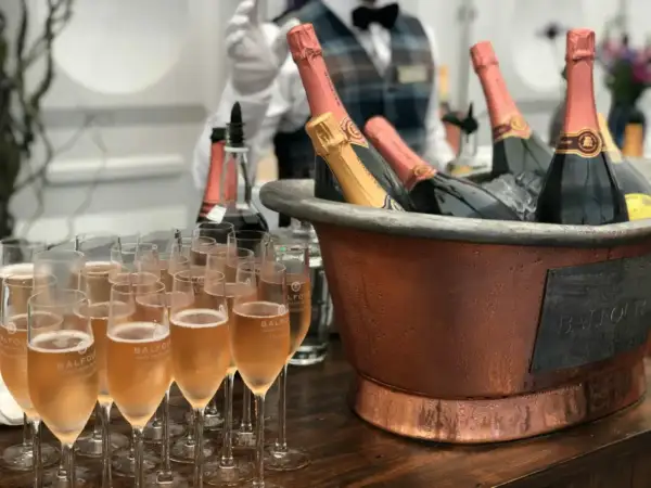 Une belle quantité de vin pour un mariage, avec des flûtes remplies de champagne et des bouteilles au frais dans un grand seau en cuivre.