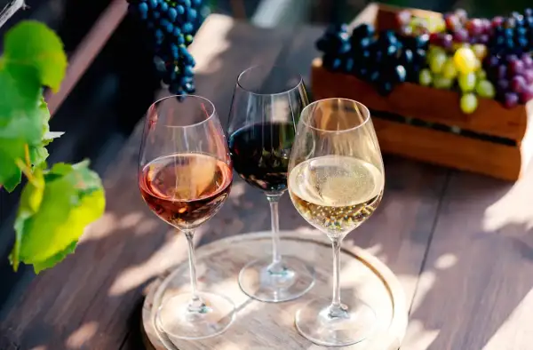 Trois verres de vin, un rosé, un rouge et un blanc pétillant, évoquent la dégustation de grands crus bordeaux, avec des grappes de raisin en arrière-plan.
