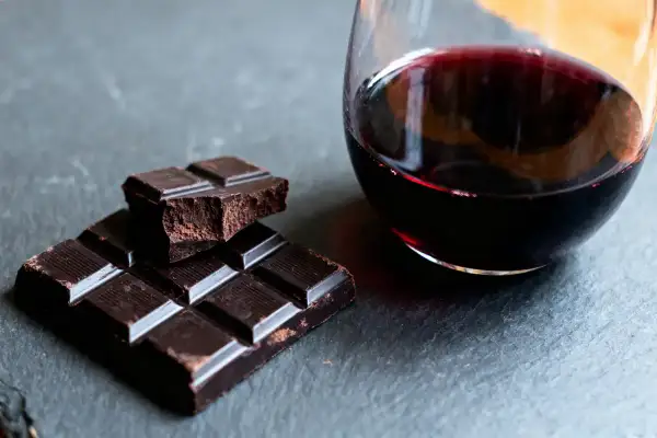 Un verre de vin rouge et des carrés de chocolat noir sur une surface sombre. Un délice pour les sens, le vin et chocolat.