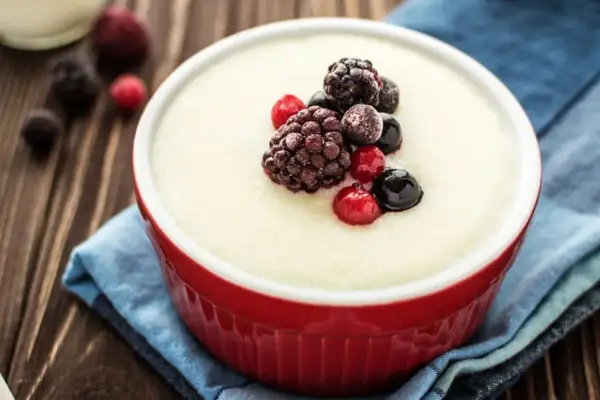 Un bol rouge de semoule au lait crémeuse, garni de baies des bois glacées. Un délice simple et réconfortant.