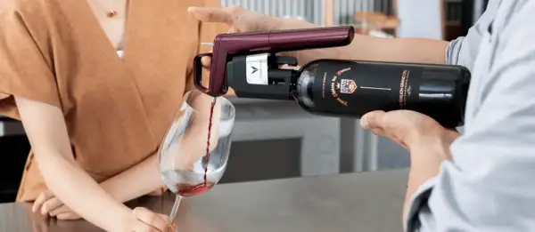 Un appareil Coravin sert un vin rouge d'une bouteille ouverte dans un verre, assurant sa conservation.