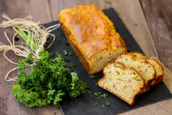 Un délicieux cake au thon, doré et moelleux, tranché et présenté avec du persil frais sur une planche d'ardoise.